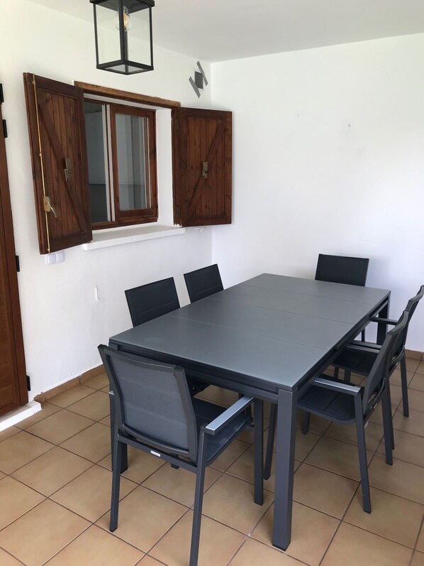 Een eetruimte met een rechthoekige tafel, zes stoelen en een raam met houten luiken.
