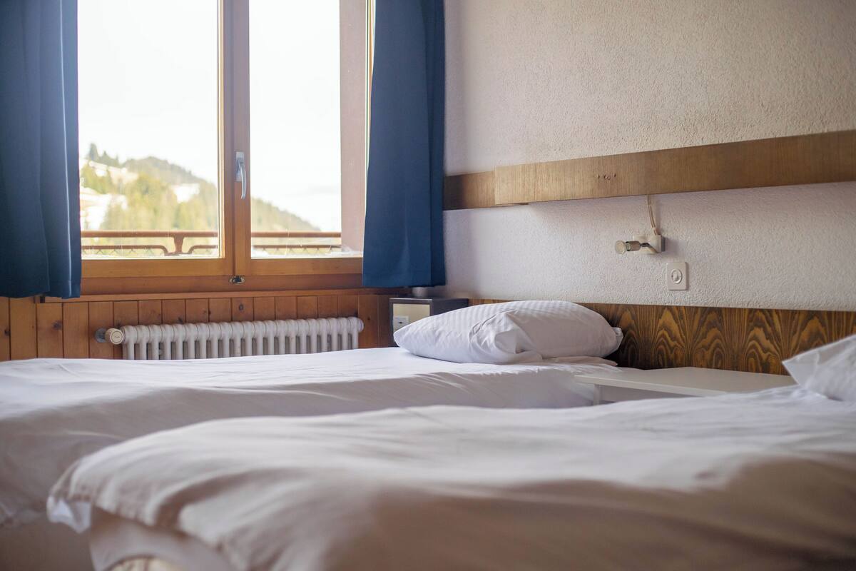 A hotel room with a wooden headboard, a white bed, a nightstand, and a window with curtains.