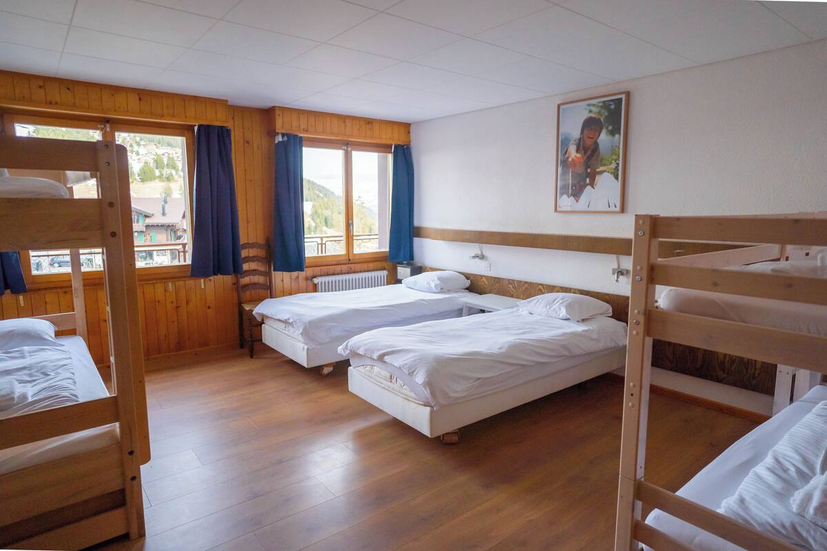 A room with bunk beds, wooden floors, a window with curtains, and a framed picture on the wall.