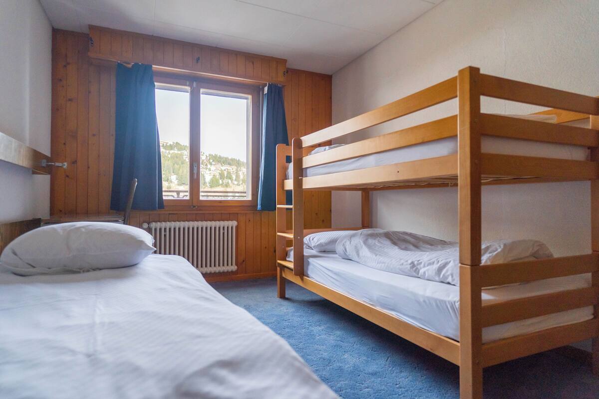 A room with two bunk beds, a window with curtains, and a radiator.