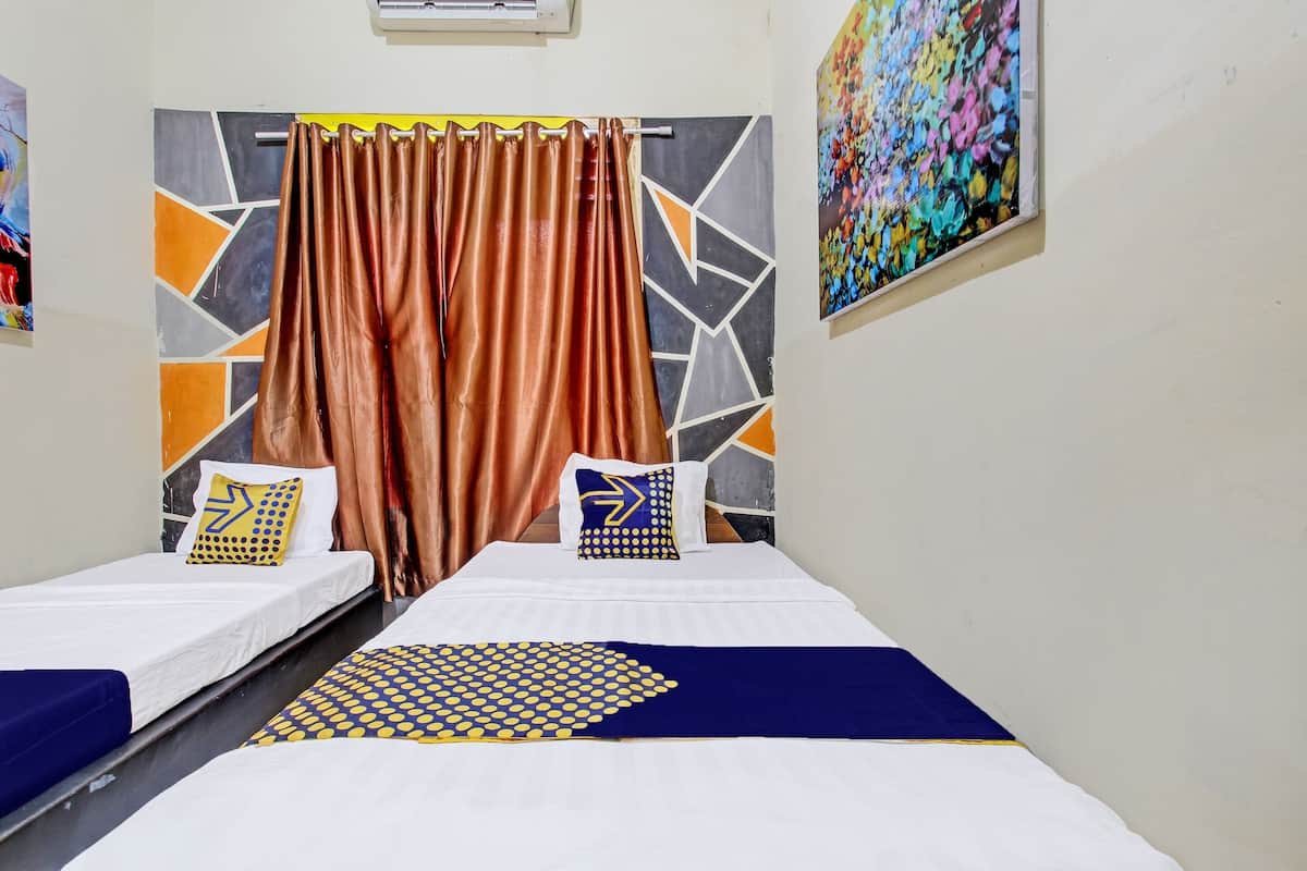 A hotel room with two single beds, each with a white mattress and blue bedding. There is a large abstract painting on the wall and a colorful artwork above the bed.