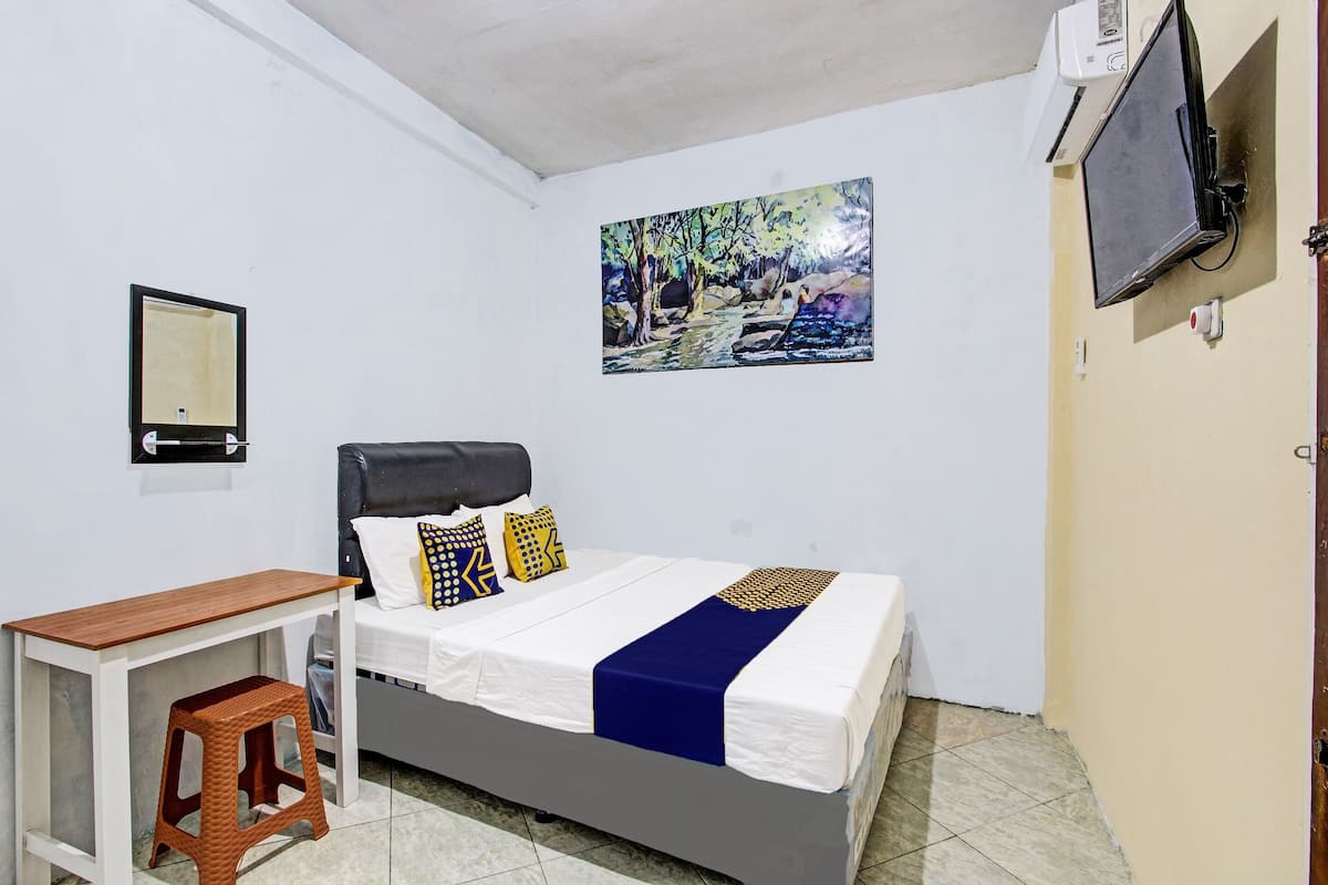 A bedroom with a bed, a desk, a stool, a painting, and an air conditioning unit.