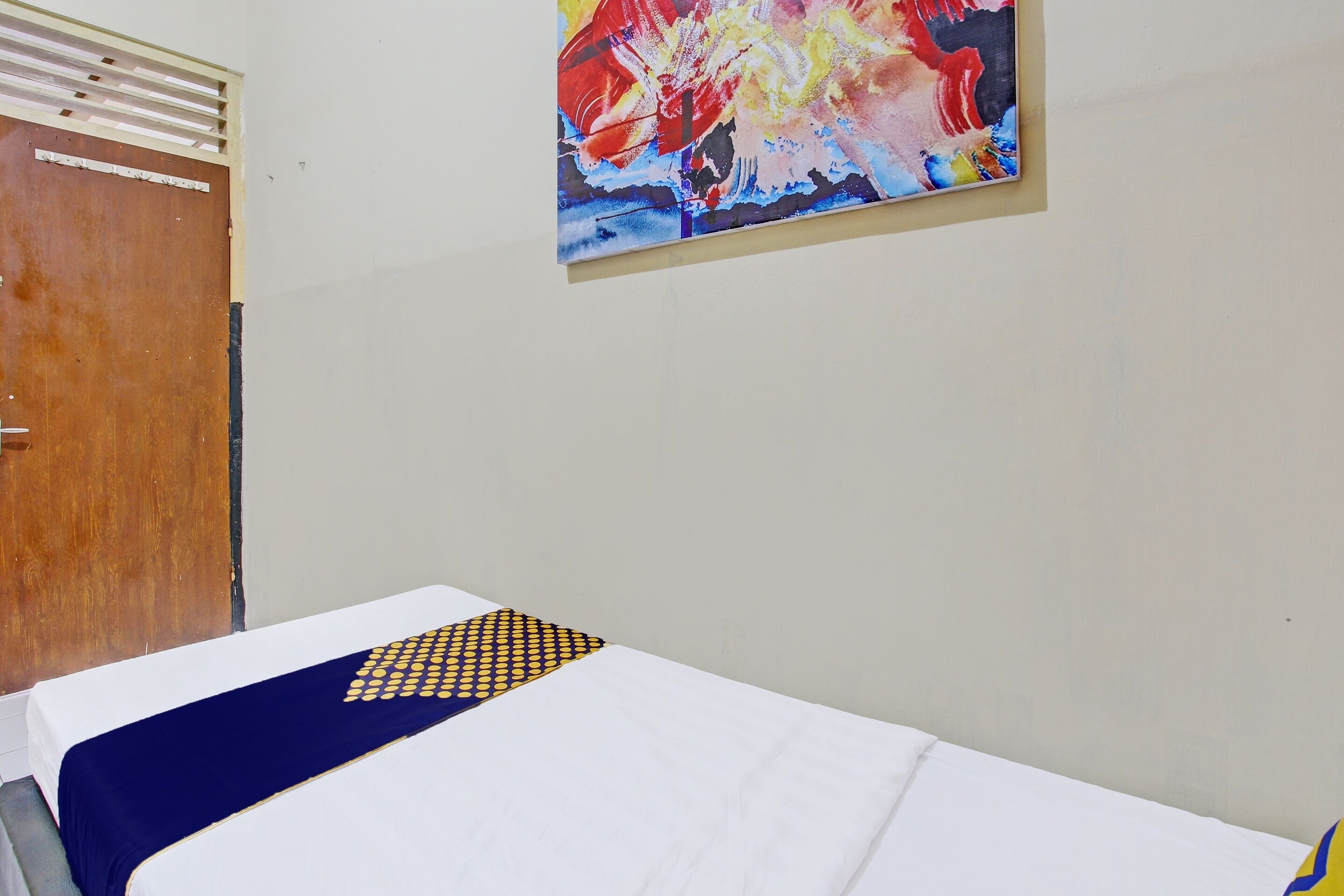 Une chambre d’hôtel avec un lit, une porte en bois et un tableau abstrait aux couleurs vives accroché au mur.