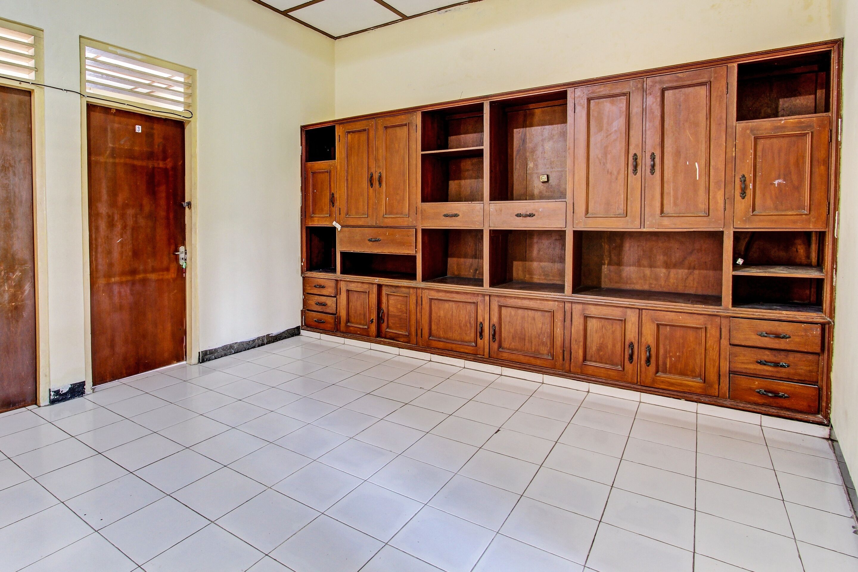 Una habitación con un gran armario de madera con varios cajones y estantes, suelo de baldosas y una puerta con ventanal.