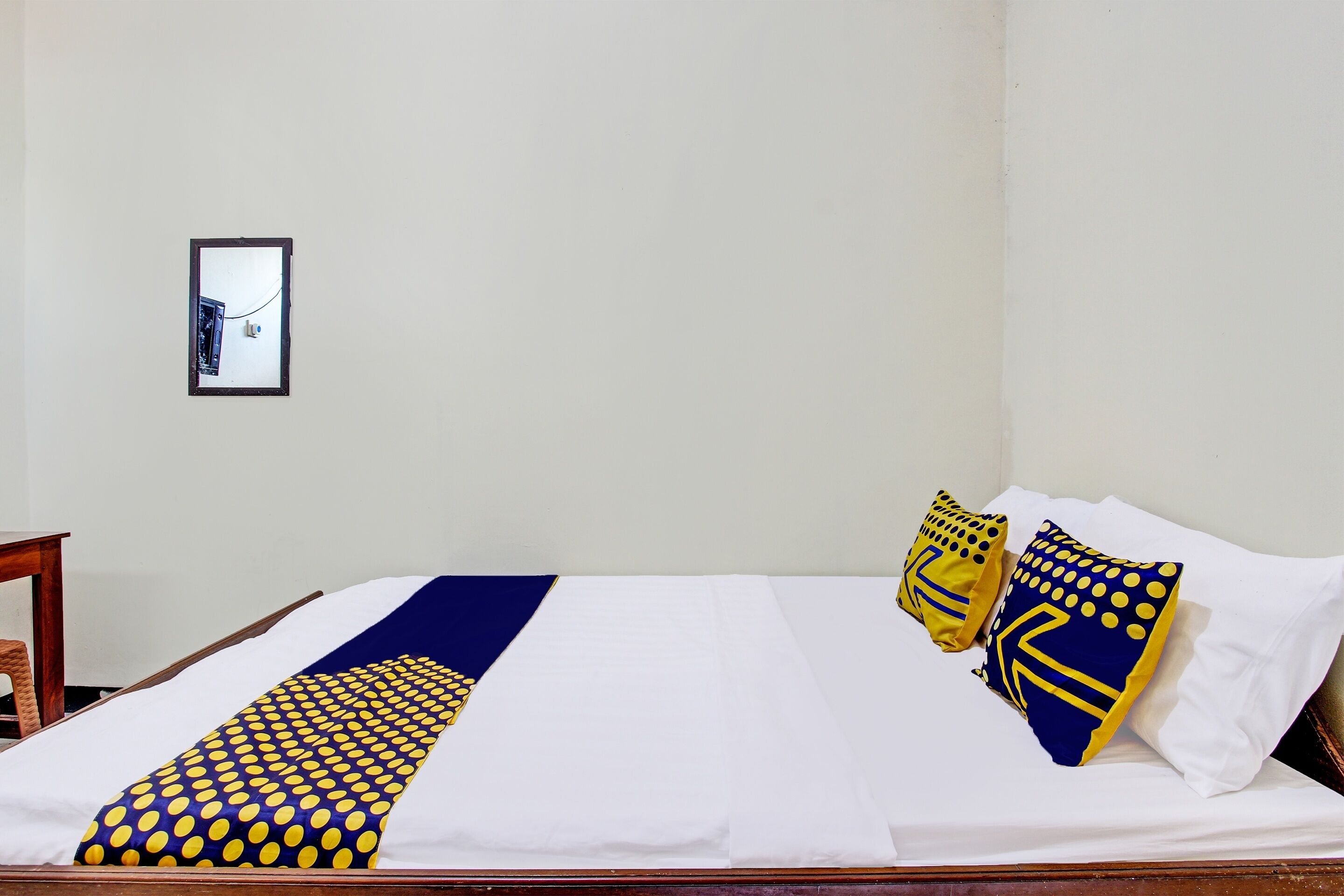 A neatly made bed with a blue and yellow patterned bedspread, two pillows with similar designs, and a framed picture on the wall.