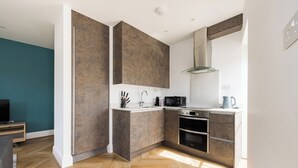 A modern kitchen with wooden cabinetry, a built-in oven, and a microwave. - Staines Riverside by Charles Hope (Staines)