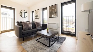 A modern living room with a grey sofa, a coffee table, and artwork on the walls. - Staines Riverside by Charles Hope (Staines)