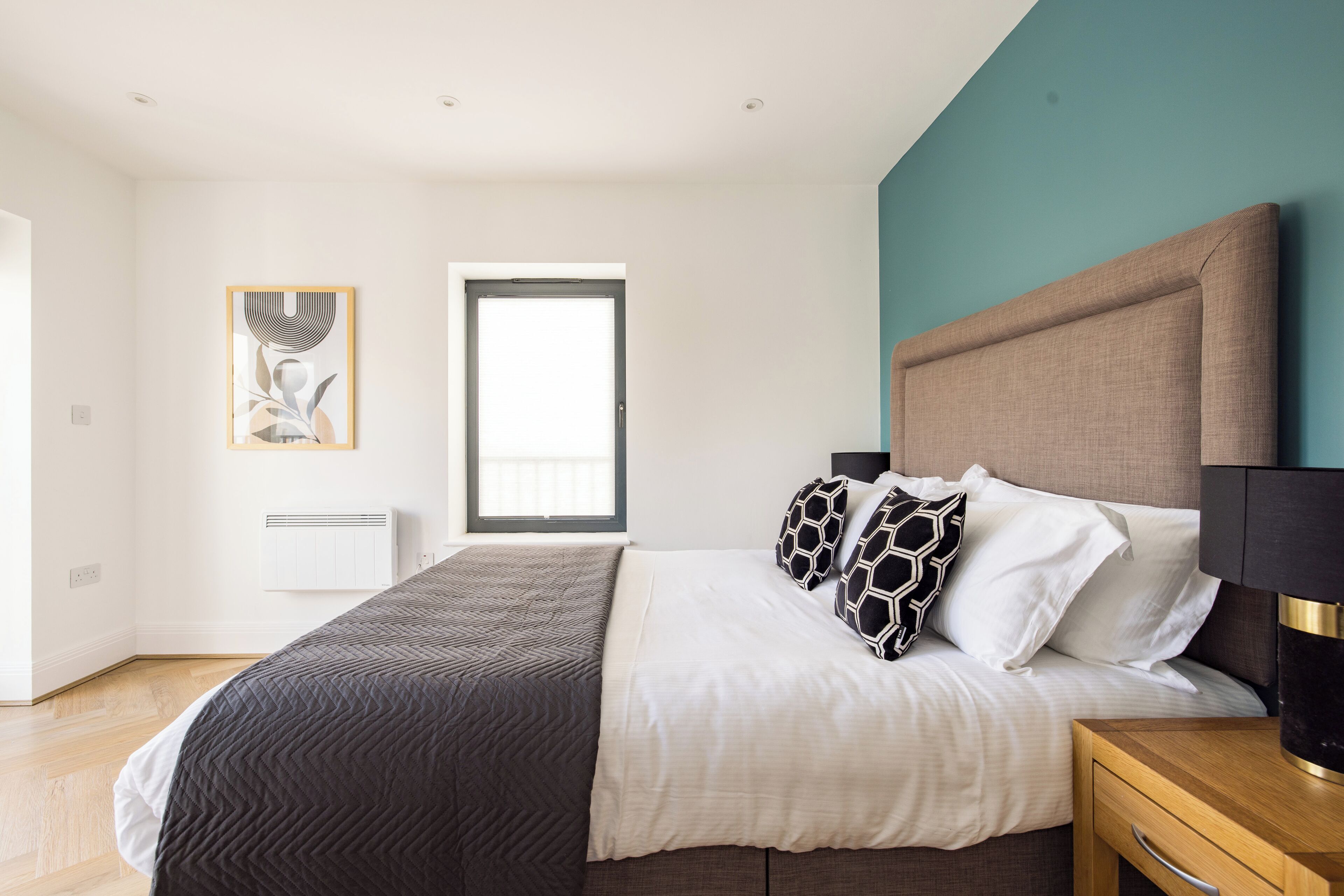 A bedroom with a bed, bedside tables, a window, and a wall-mounted artwork.
