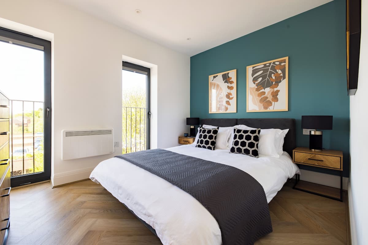 A bedroom with a large bed, a nightstand, a window with a view, and artwork on the wall.