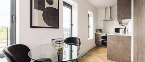 A modern kitchen with a glass dining table, black chairs, and a large abstract painting on the wall.