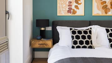 A neatly made bed with a patterned pillow, a bedside table with a lamp, and two framed artworks on the wall.