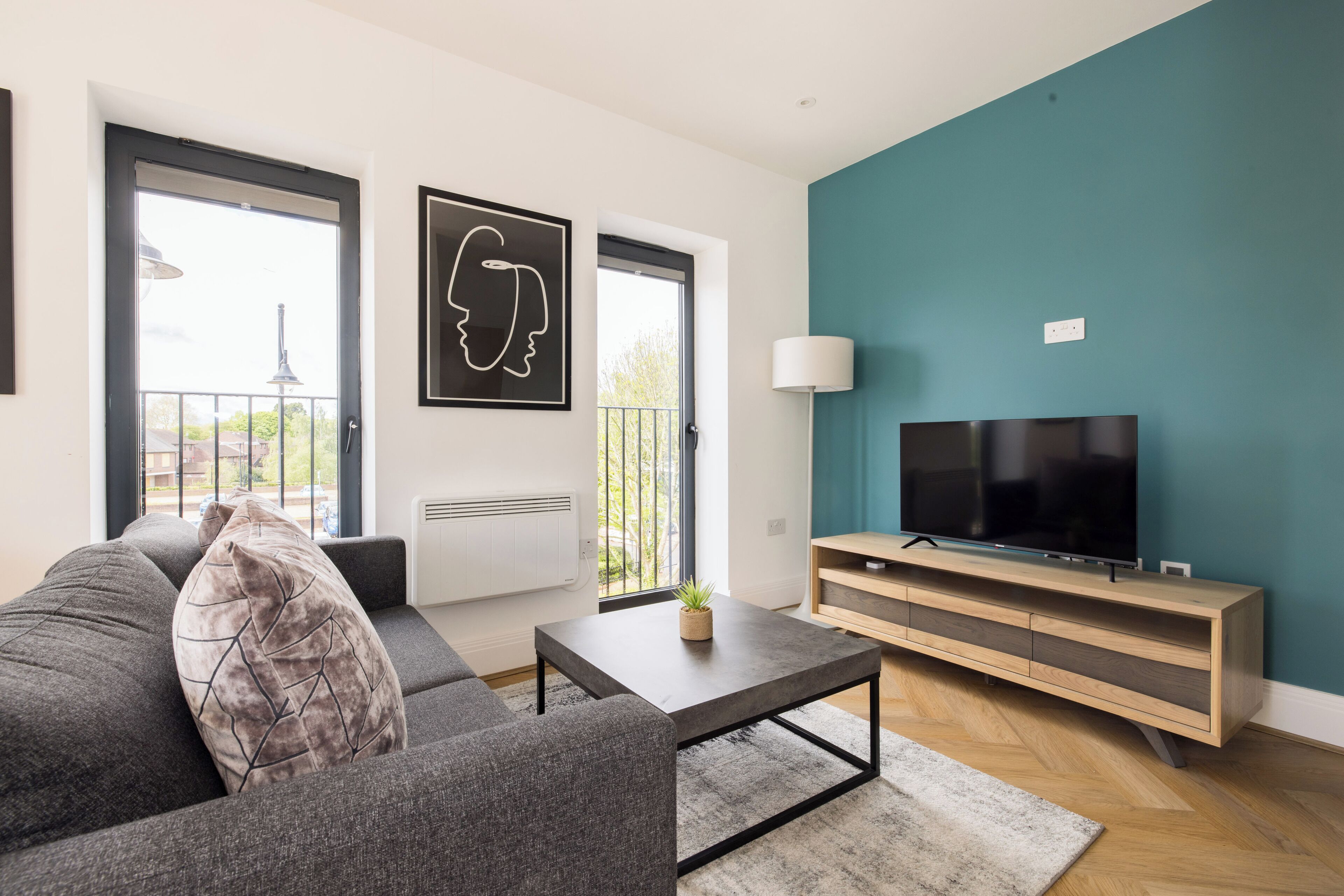 Una sala de estar moderna con un sofá, una mesa de centro, un televisor sobre un mueble de madera y vistas a través del ventanal.