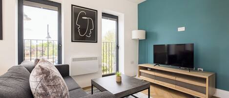 Un salon moderne avec un canapé, une table basse, un téléviseur posé sur un meuble en bois et une vue par la fenêtre.