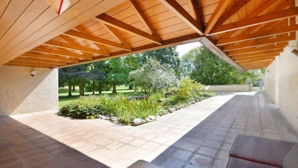 Un espace patio extérieur doté d’une structure de plafond en bois, d’un revêtement de sol en pierre et offrant une vue sur un jardin aménagé.