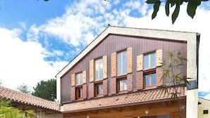 Une maison moderne avec un bassin devant, entourée de plantes et de rochers.