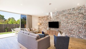 Een moderne woonkamer met een bakstenen muur, een flatscreen televisie, een bank en een eetgedeelte met een tafel en stoelen.