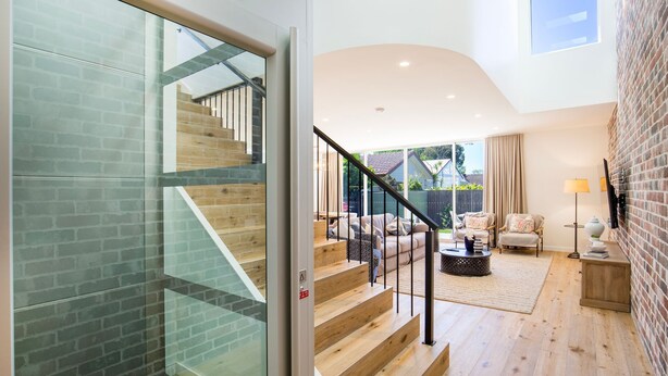 Een modern interieur met een trap die naar een balkon leidt, een zithoek met een bank en salontafel, en een bakstenen muur.
