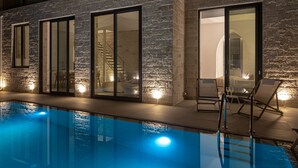 A modern indoor pool area with stone walls and glass doors, equipped with lounge chairs and a clear pool. - Perla Dream Luxury Villa (Chania)
