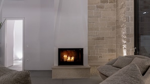 A modern living room with a fireplace, stone wall, and comfortable seating. - Perla Dream Luxury Villa (Chania)