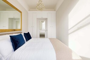 Quarto com cama grande, espelho, lustre e paredes brancas.