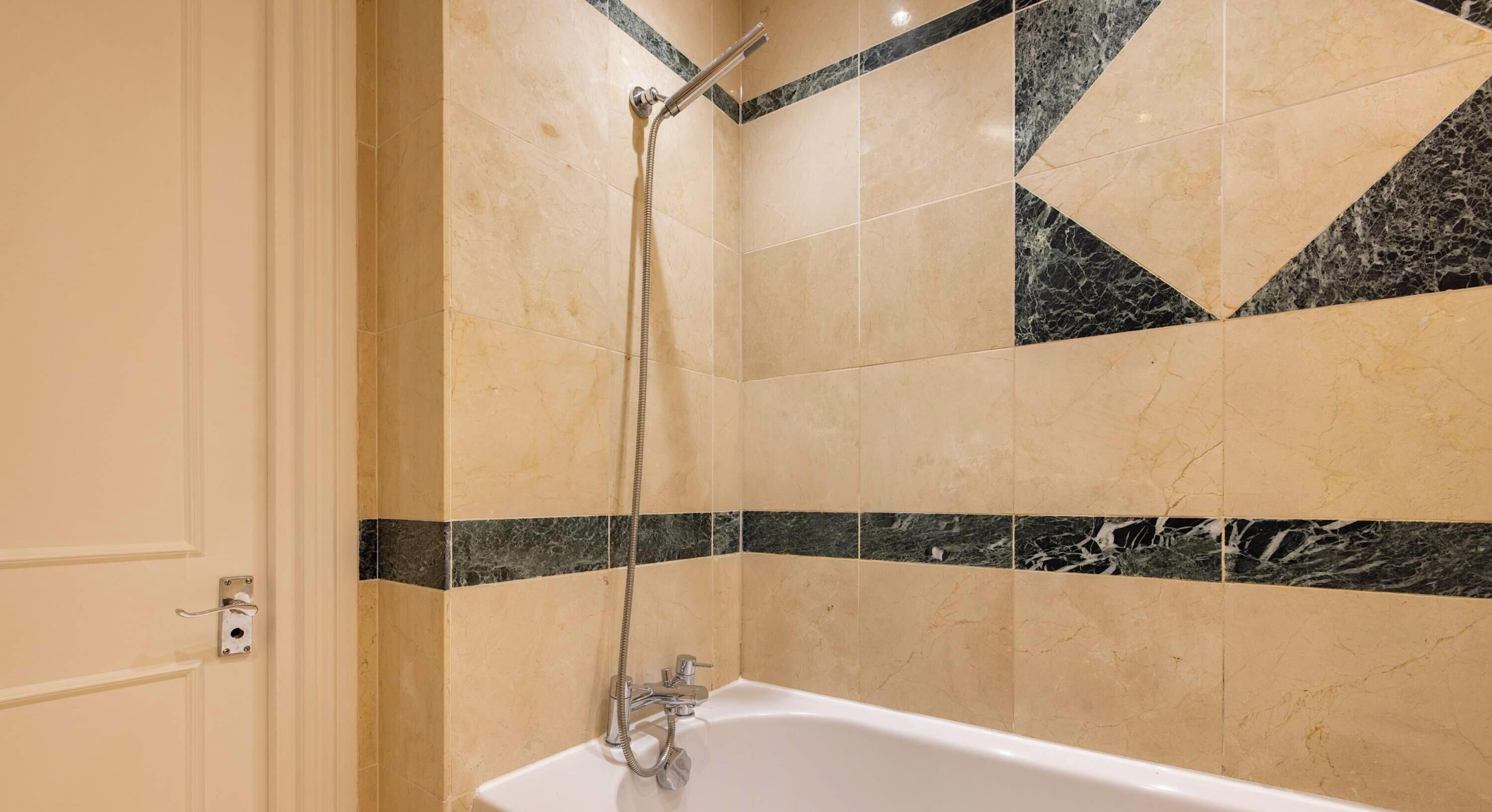 A bathroom with a bathtub, a shower, and a tiled wall with a geometric pattern.