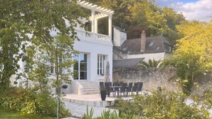 Una casa moderna con fachada blanca, un porche cubierto y un jardín con un banco de metal.