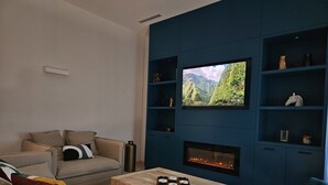 Una sala de estar moderna con chimenea, un televisor montado en una pared azul y un rincón de descanso acogedor con sofá y sillones.