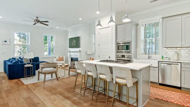 A modern kitchen with white cabinets, a central island with bar stools, a built-in oven, and a dishwasher. - Shem Creek House- 5 Mins to Dtwn & Beach Hot Tub (Mount Pleasant)