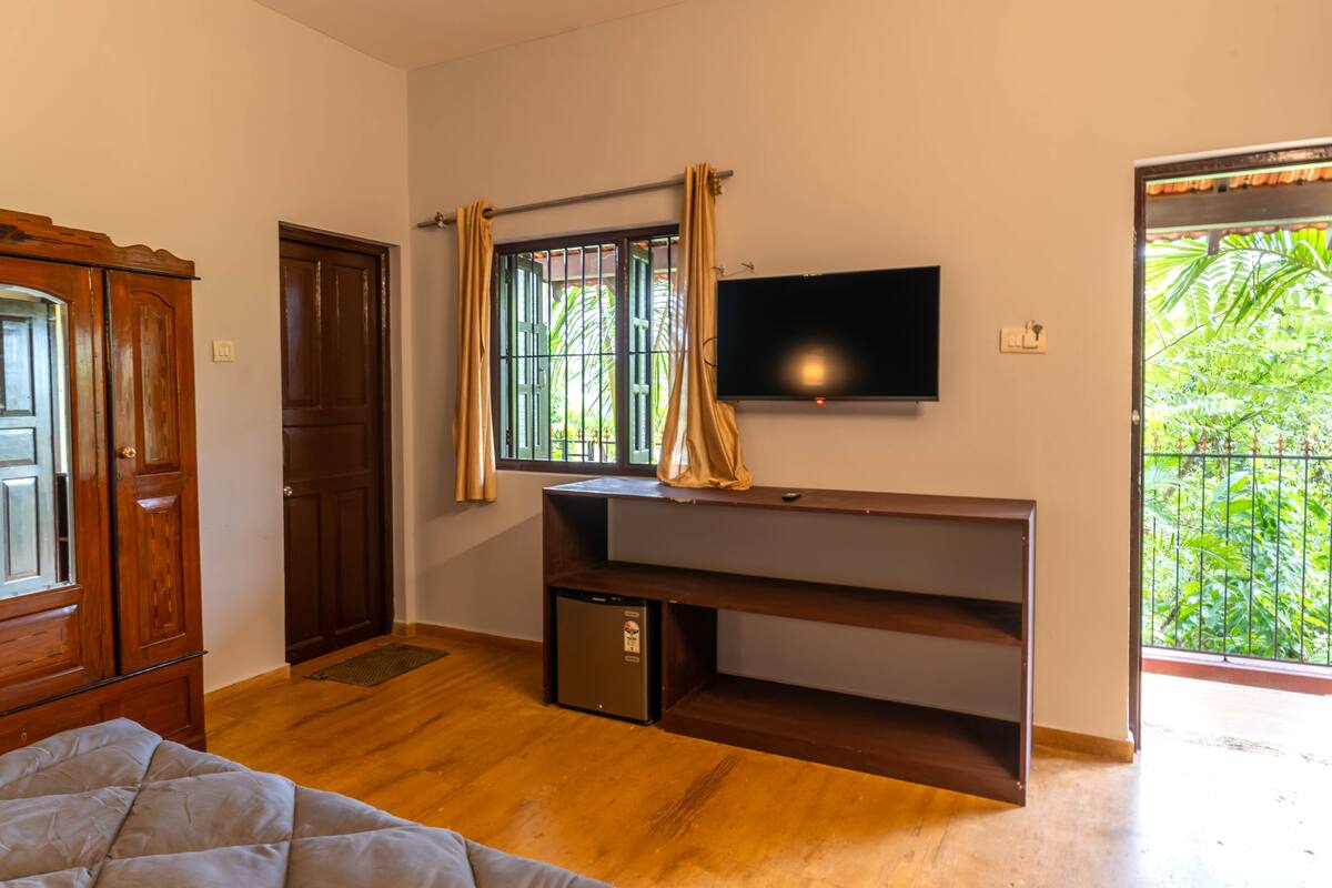 Una habitación con cama, televisión montada en la pared, refrigerador pequeño y ventana con cortinas.