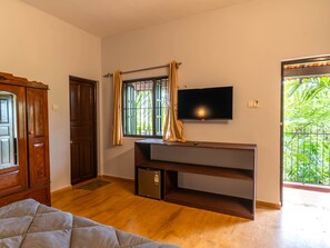 Una habitación con cama, televisión montada en la pared, refrigerador pequeño y ventana con cortinas.