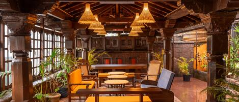 A cozy restaurant interior with wooden furniture, hanging wicker lamps, and potted plants.