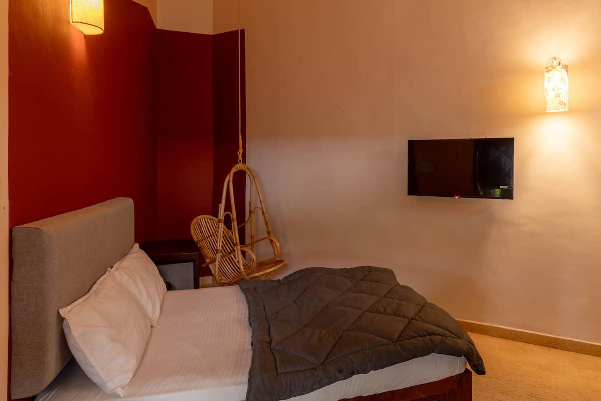 Un dormitorio con cama, una silla colgante, un televisor montado en la pared y una lámpara de pared.
