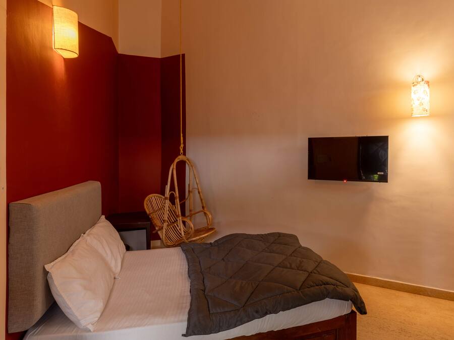 Un dormitorio con cama, una silla colgante, un televisor montado en la pared y una lámpara de pared.