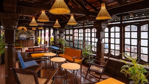 A restaurant interior with wooden furniture, hanging wicker lamps, and large windows.