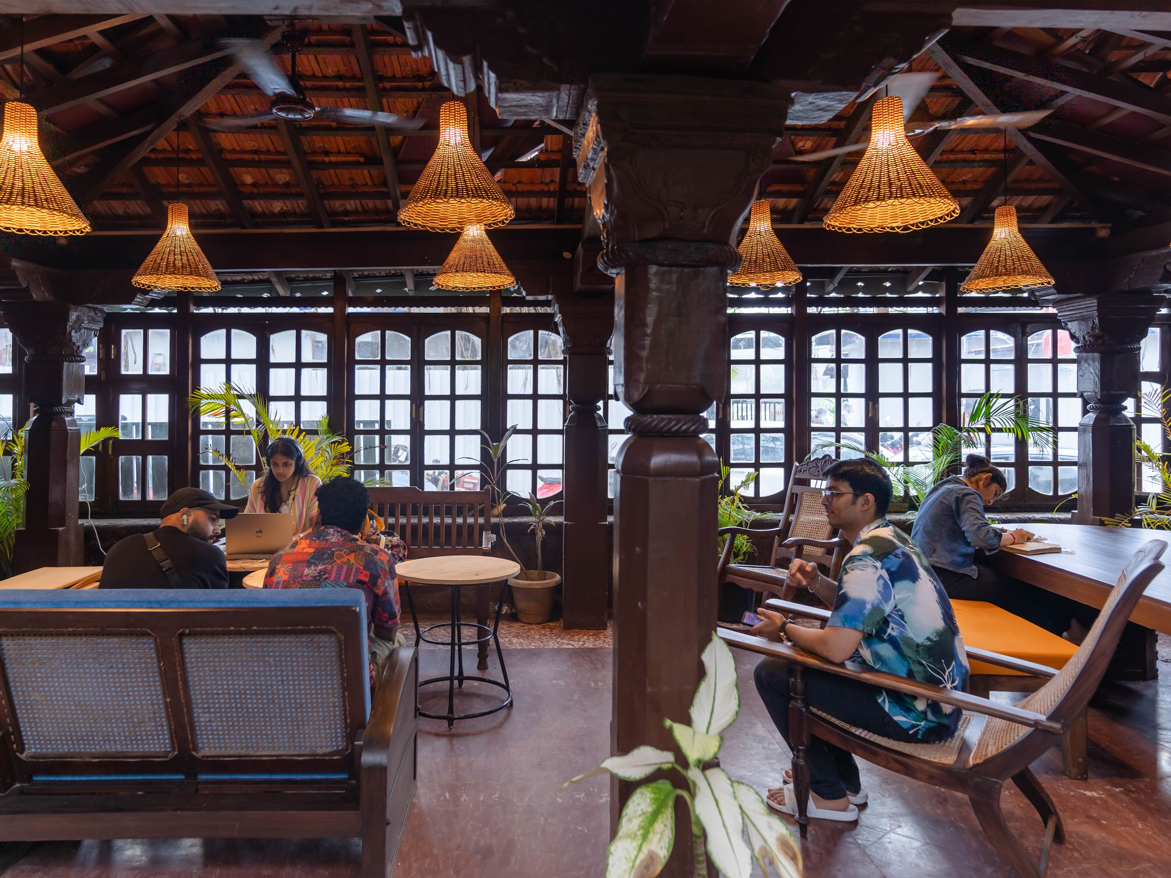 A restaurant with wooden furniture, hanging wicker lamps, and large windows.