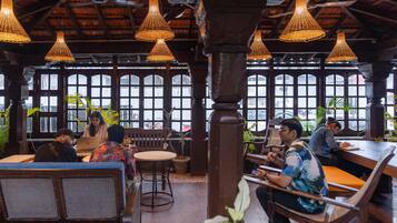 A restaurant with wooden furniture, hanging wicker lamps, and large windows.