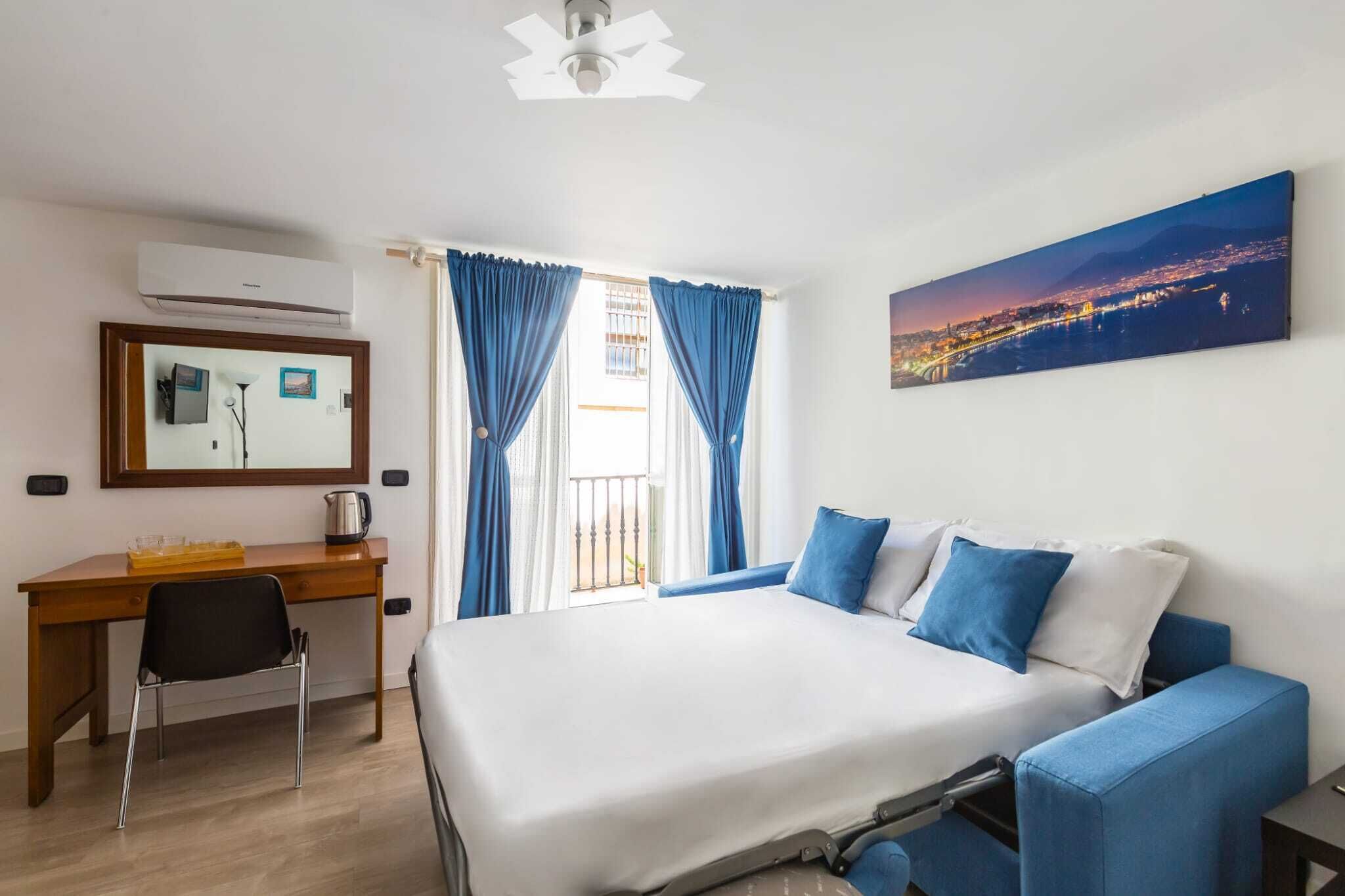 Habitación de hotel con cama, escritorio, silla, cafetera y un cuadro de un paisaje urbano.