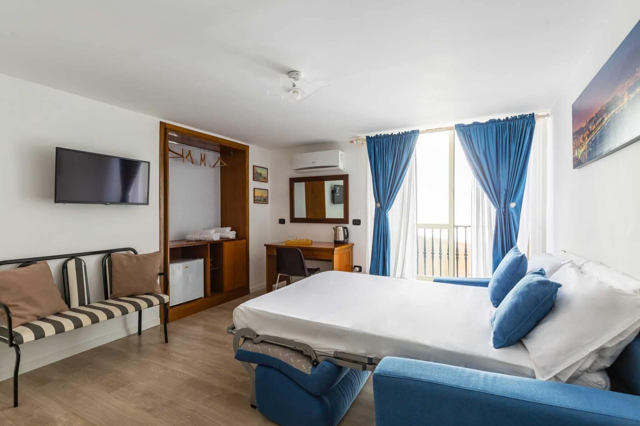 A hotel room with a bed, a sofa, a desk, a TV, and a wardrobe.