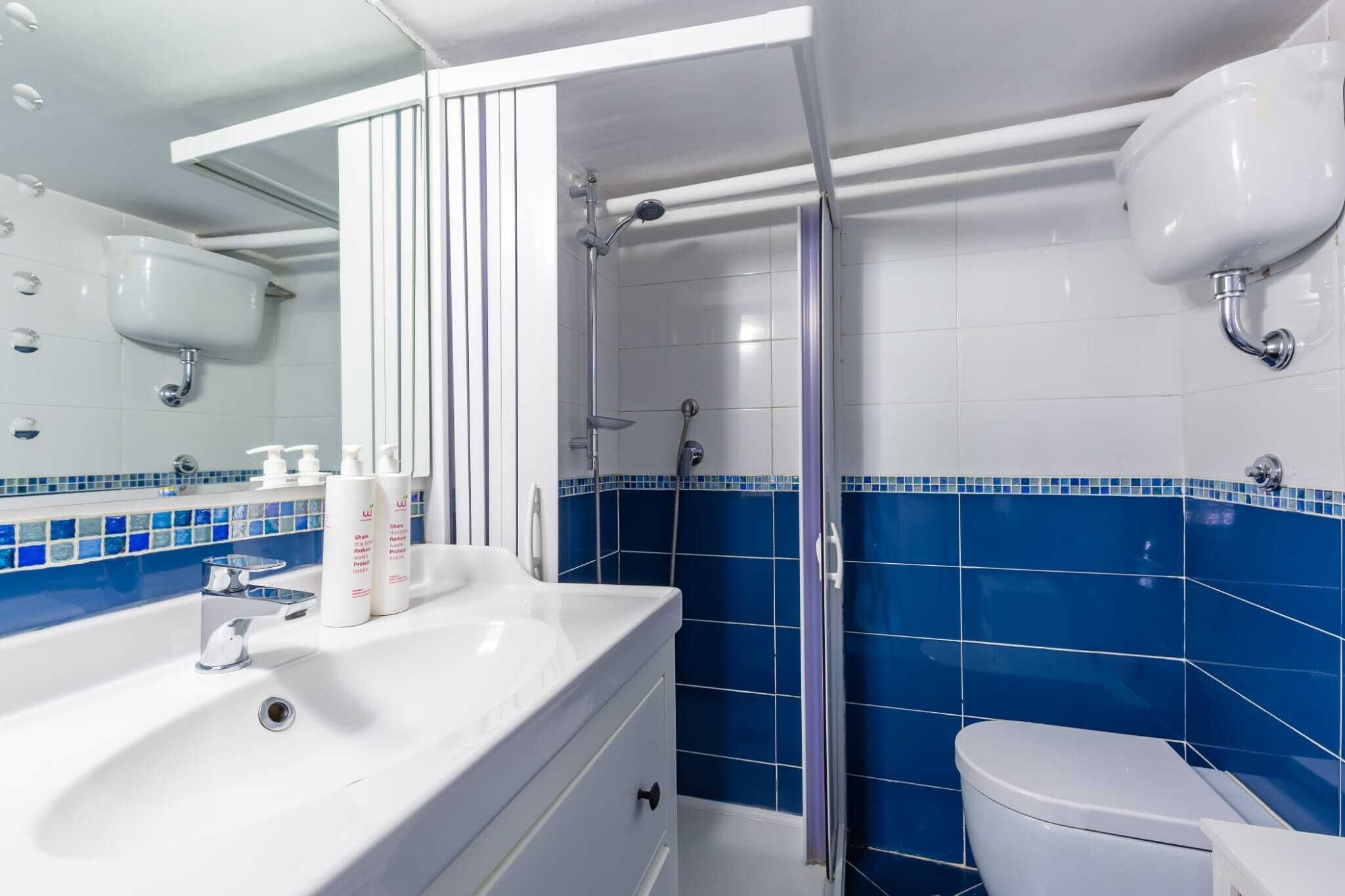 A bathroom with a white sink, blue-tiled walls, a shower, and a toilet.