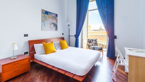 Ett hotellrum med en säng, ett skrivbord, en stol, ett nattduksbord och ett fönster med gardiner.