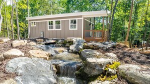 A cabin with a small waterfall, surrounded by rocks and trees. - Romantic Beehive Treehouse Getaway in Nature (Pittsboro)