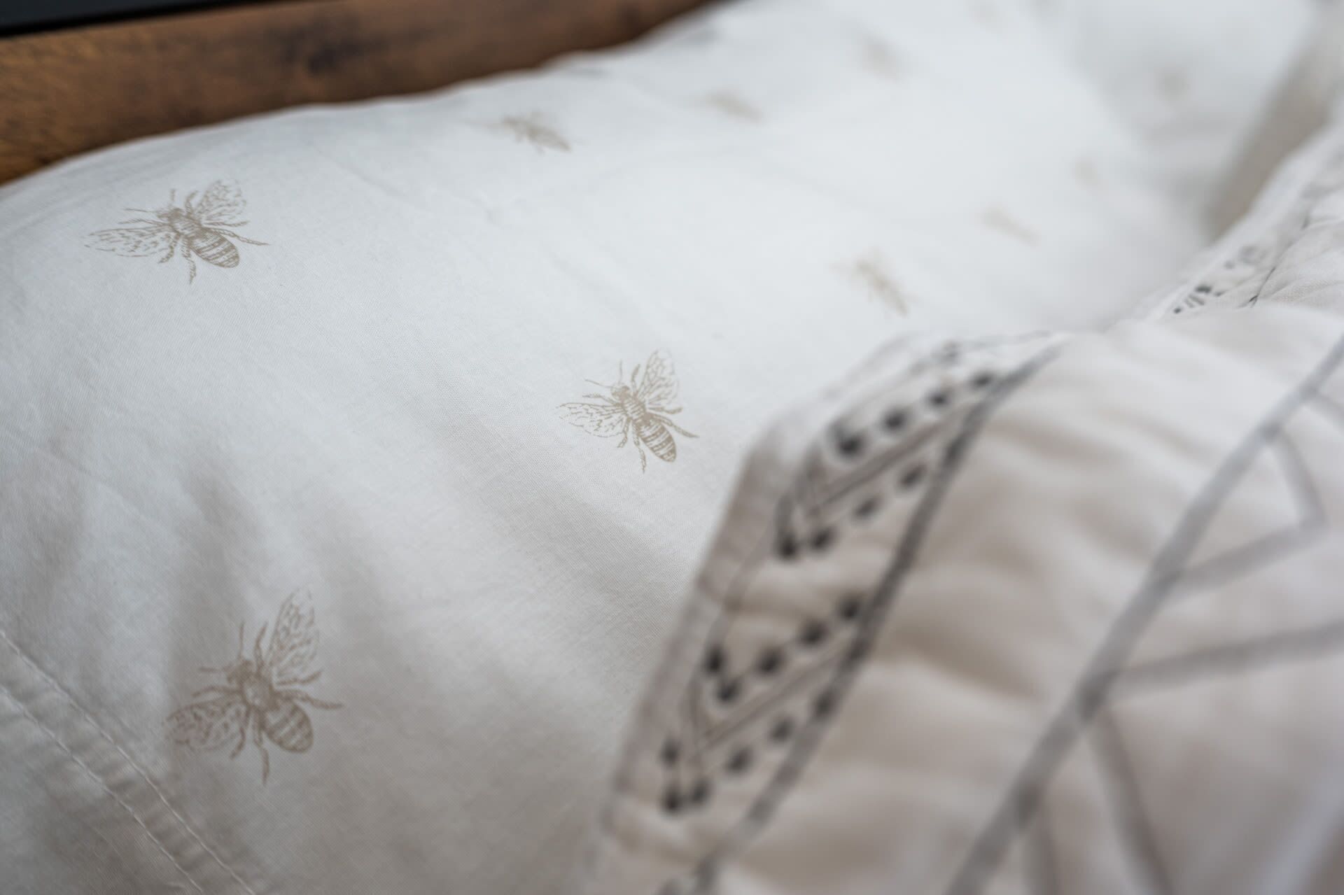 Un letto con lenzuola bianche decorate con api ricamate e un bordo decorativo.