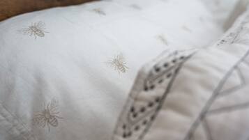 Un letto con lenzuola bianche decorate con api ricamate e un bordo decorativo.