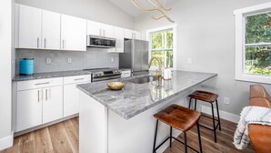 A modern kitchen with white cabinets, a large island, and a view of greenery outside.