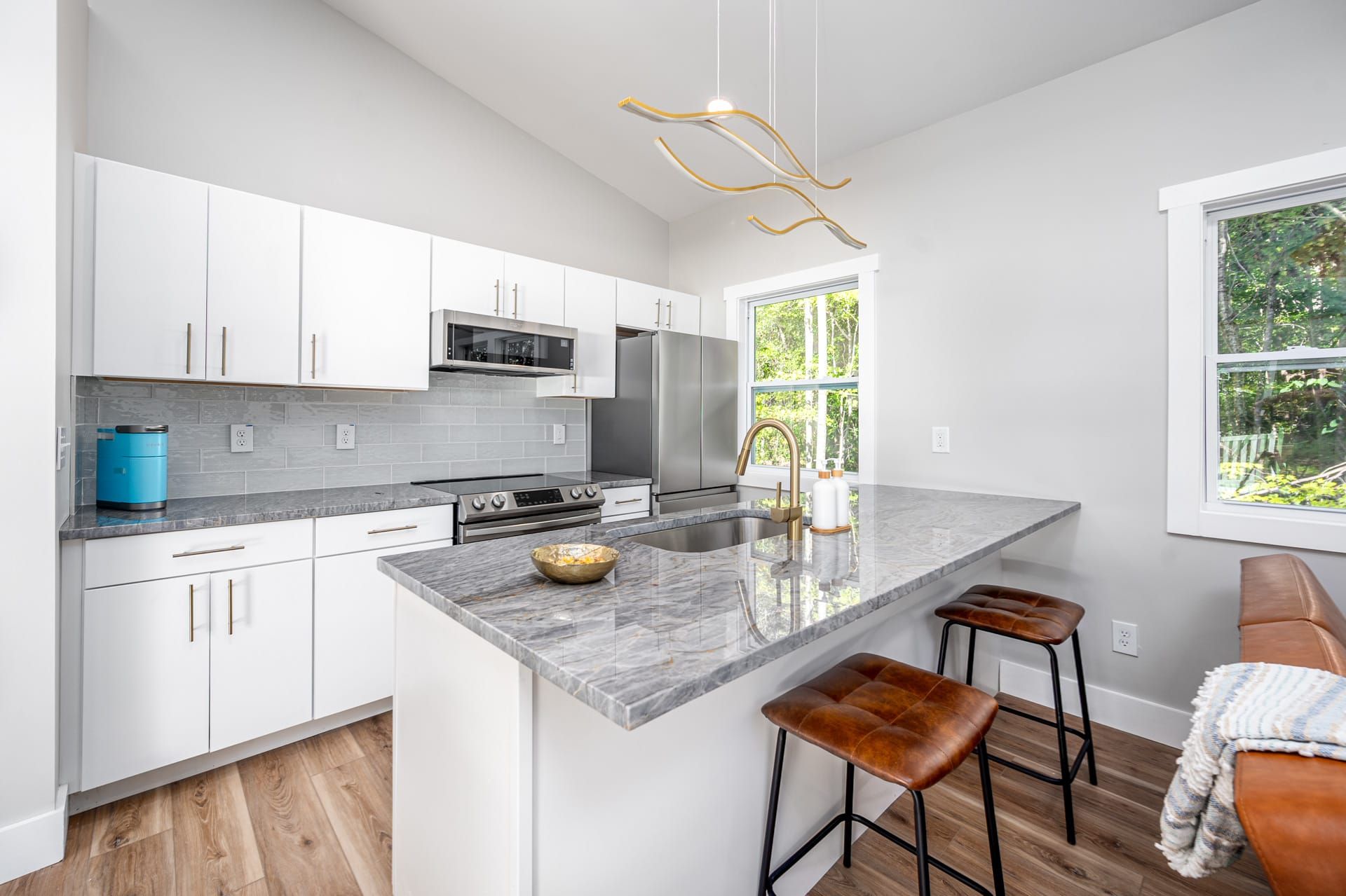 A modern kitchen with white cabinets, a large island, and a view of greenery outside.