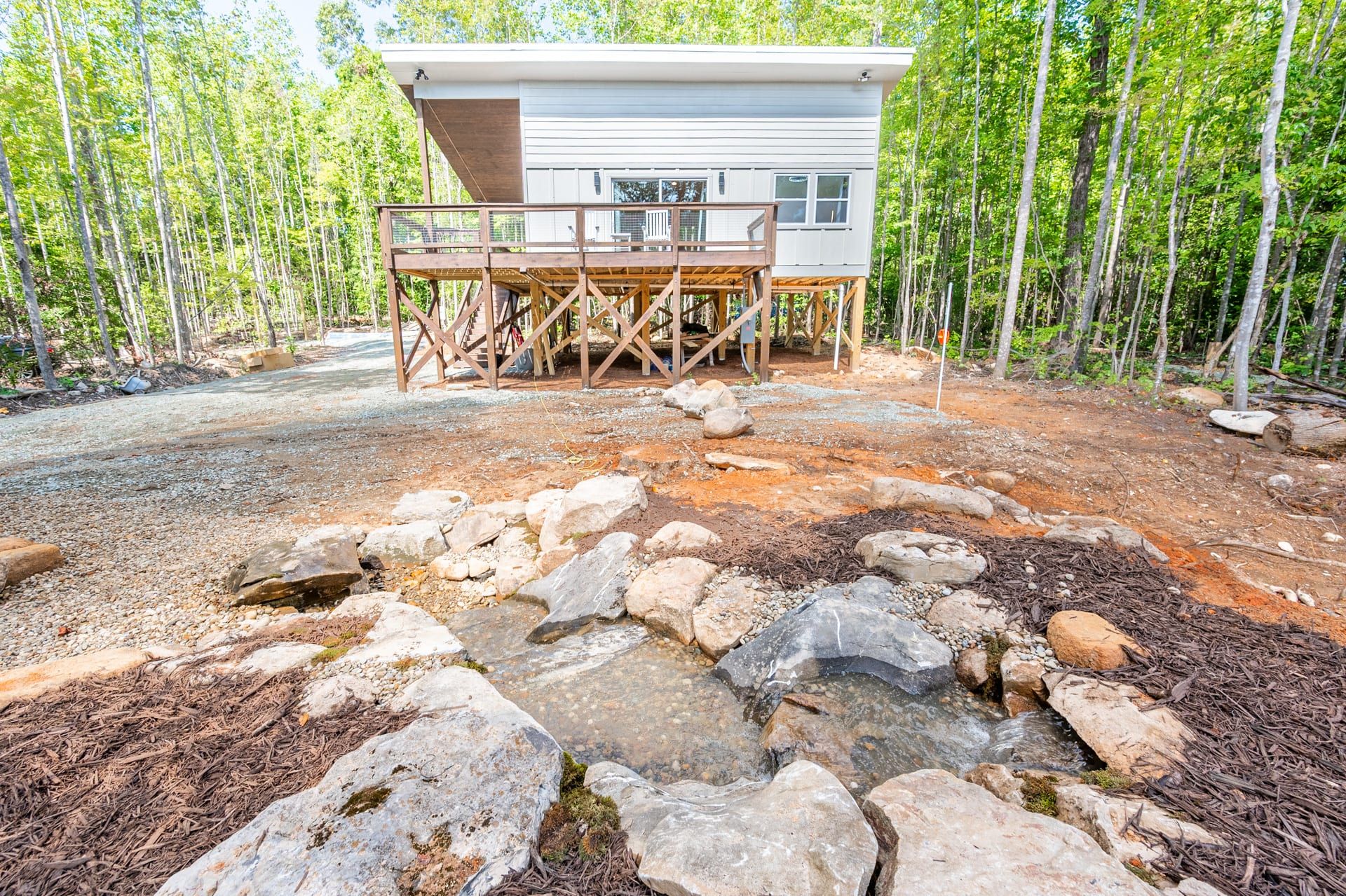 Une cabane dotée d’une terrasse, entourée d’une forêt et bordée d’un ruisseau aux rochers.