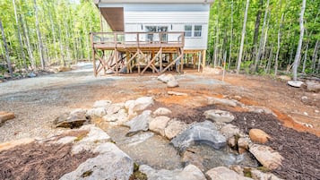 Une cabane dotée d’une terrasse, entourée d’une forêt et bordée d’un ruisseau aux rochers.