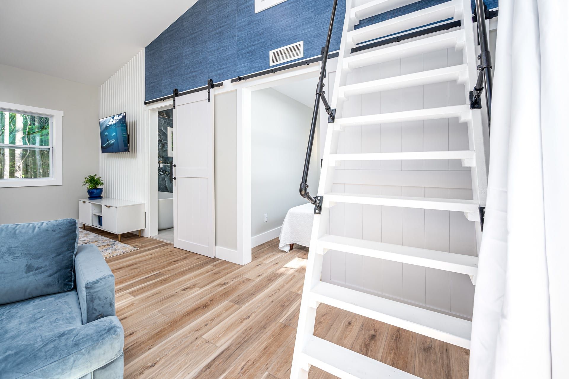 A modern interior with a blue accent wall, a white ladder, and a blue sofa.