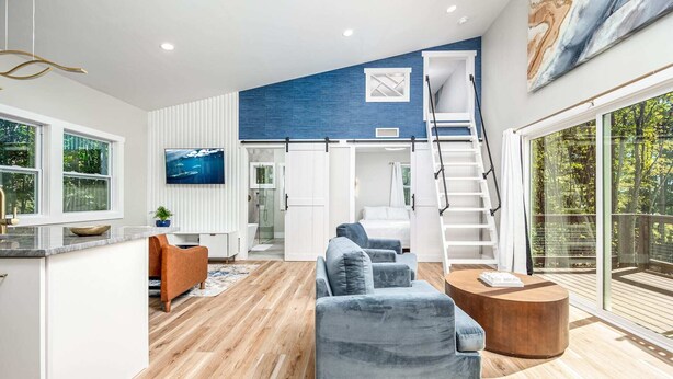 A modern interior with a living area, kitchen, and a staircase leading to a balcony.