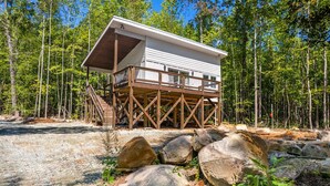 A cabin with a wooden deck and a covered upper level, surrounded by a forest.